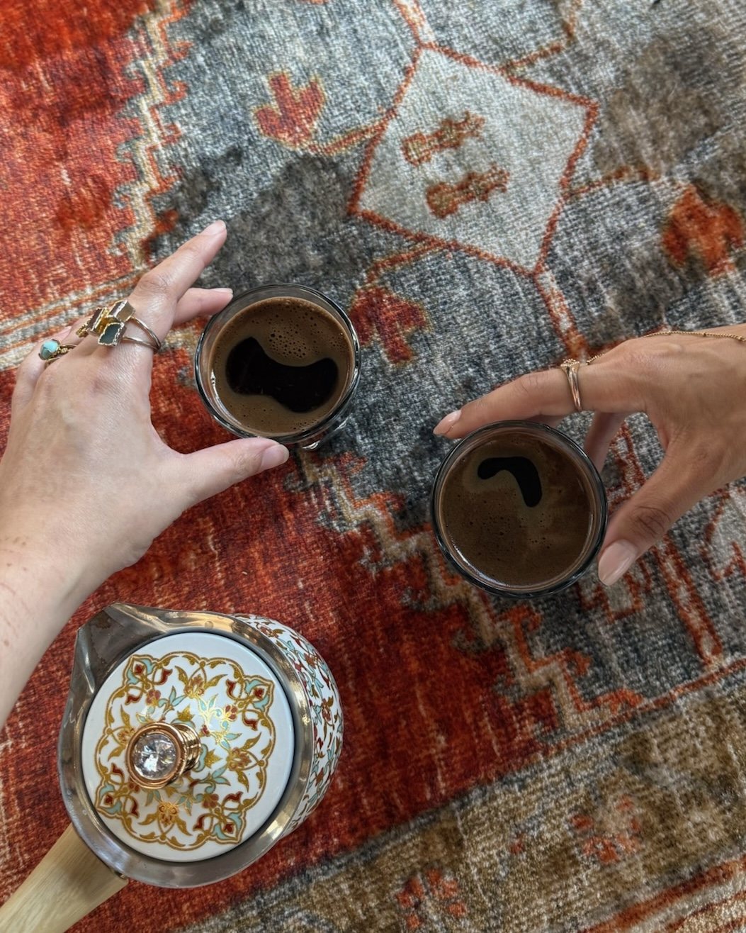Hands sharing Turkish coffee over a vintage rug