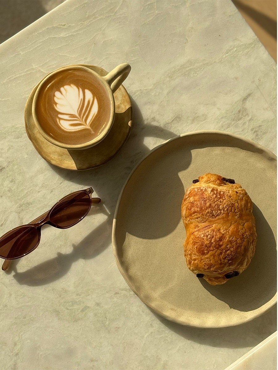 Latte and chocolate croissant with sunglasses on a stone table