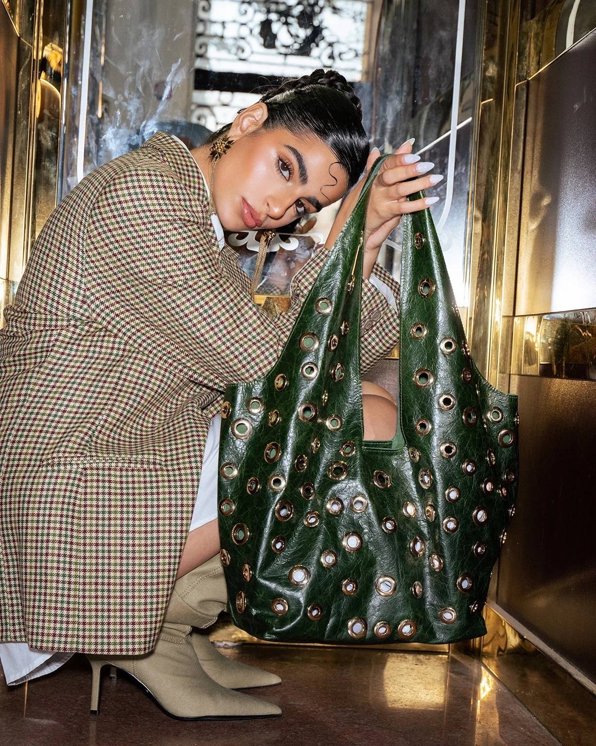 Sally Antar green grommet-studded leather bag, held in a gold-mirrored elevator