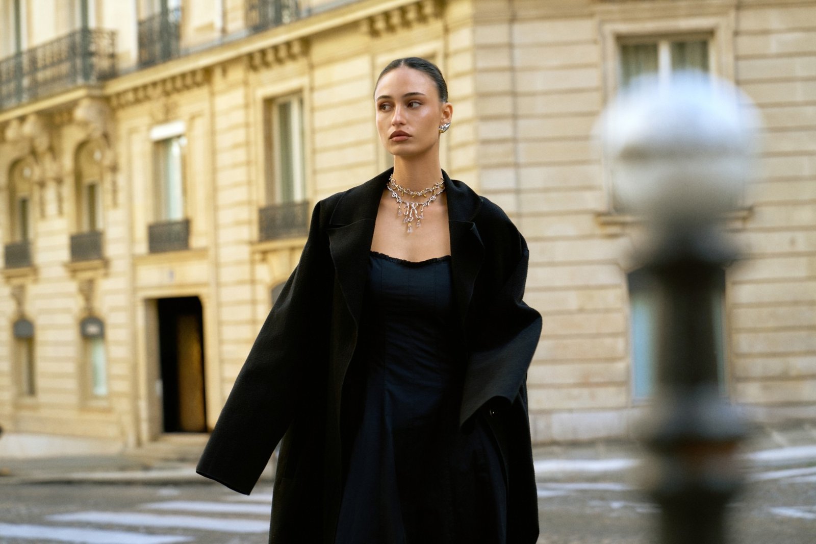 Statement necklace over a black coat, city street editorial